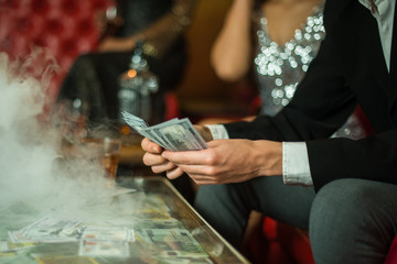 Man with cigar counting money in the club. Group of young multi-ethnic friends relaxing in shisha club-bar in rich interior