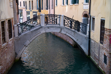 Ponte de le Colonne, on the Rio dei Fuseri. Calle dei Fuseri, Venice, Italy. Stone bridge; brick and stone structure, iron balustrades with oblique crosses and circles.