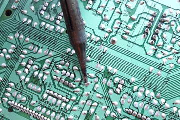 A soldering iron plated tip soldering a through hole component on its track on a green printed circuit board