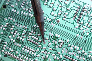 A soldering iron plated tip soldering a through hole component on its track on a green printed...