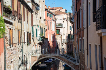 Fototapeta na wymiar Typical Venetian buildings with canal and bridge in Venice, Italy. Old houses along the banks of water with boats.