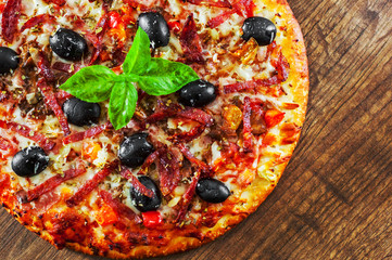 Pizza with Mozzarella cheese, salami, pepper, ham, pepperoni, olives, Spices and Fresh Basil. Italian pizza on wooden background