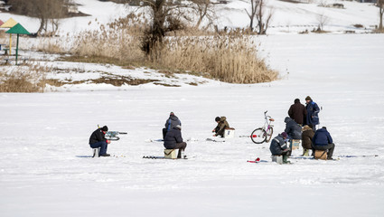 Fishermen on ice fishing on a frozen pond in sunny weather. Selective focus.