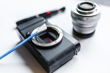 Close-up of mirrorless digital APS-C dirty camera matrix sensor cleaning and maintenance with swab, photographer cleaning photocamera on white background