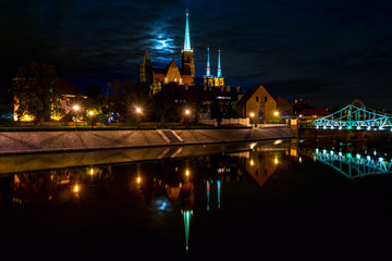 Obraz premium Reflection scenic with moon view of the Old Town architecture and Oder river embankment and historical district Ostrow Tumski with the spires illuminated of the gothic cathedral in Wroclaw, Poland