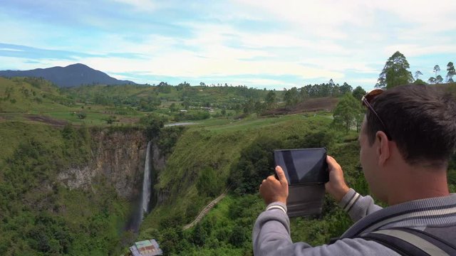 Cinemagraph of Young Man Taking Photo of Sipiso Piso Waterfall, North Sumatra, Indonesia. Male Traveler Living Active Lifestyle