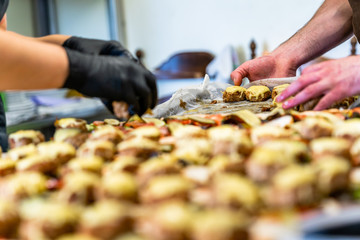 Female and Male Chef Putting Ingredients of Burgers on a Sliced Bread Spread on a Table in Black Gloves