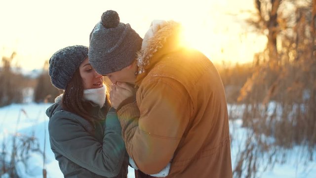 Love story, a boyfriend warming girlfriend hands in winter park.