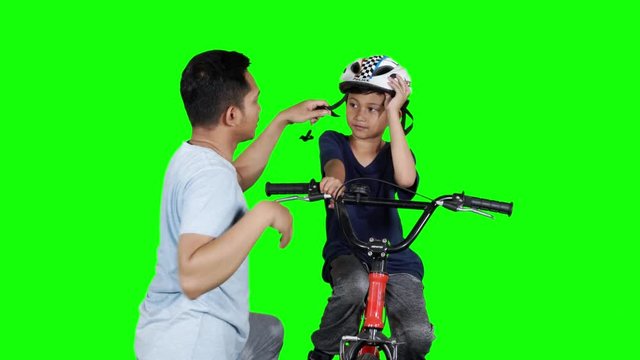 Young man helping his son to wear helmet before riding bicycle. Shot in 4k resolution with green screen background