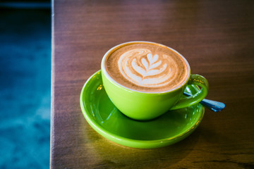 cappucino in a green cup and saucer with foram art in the shape of a leaf
