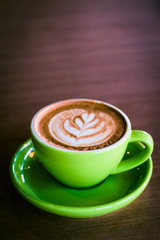 cappucino in a green cup and saucer with foram art in the shape of a leaf