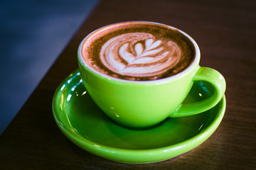 cappucino in a green cup and saucer with foram art in the shape of a leaf