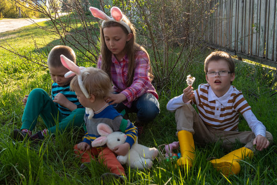 Cute village children wearing bunny ears on Easter day. Child holds basket with painted eggs. Green grass and flowering trees. Boys and girl are happy together.