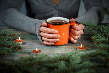 Fototapeta na wymiar Woman holds a cup of hot tea among the fir branches and candle.