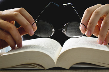 Male hand holding eyeglasses on open book.