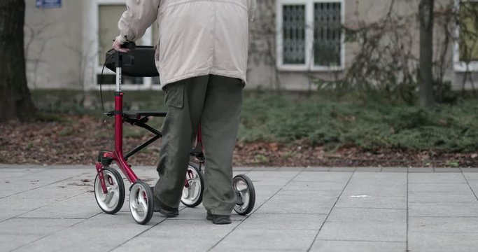 Old man walking on the city street with his red color walker. 4K Footage - Video
