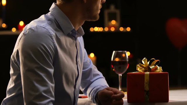 Frustrated boyfriend putting gift on table and leaving restaurant, break-up