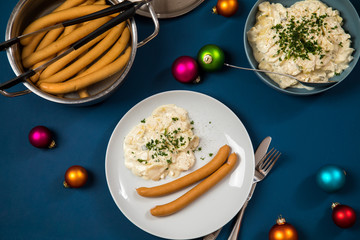 Wiener Würstchen und Kartoffelsalat als typisches Weihnachtsessen zu Heiligabend in Deutschland mit bunten Weihnachtsbaumkugeln und Dekoration