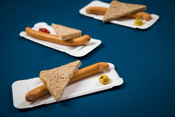 Fototapeta premium Wiener Würstchen mit Vollkorn Brot Scheibe auf Einweg Pappteller mit Senf und Ketchup auf Hintergrund Blau