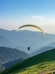 Yellow paraglider in blue clear sky over the Green Mountain