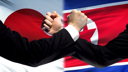 Japan vs North Korea confrontation, interests conflict, fists on flag background