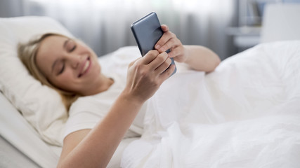 Obraz na płótnie Canvas Cheerful teenage girl just woke up and using smartphone to surf internet