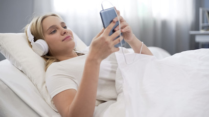 Teenager in headphones listening to music in bed, communicating in social media