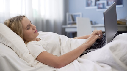 Teenager lying in bed with laptop, choose virtual communication instead real