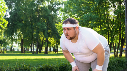 Obese man running outdoors, out of breath, overcoming laziness and insecurity