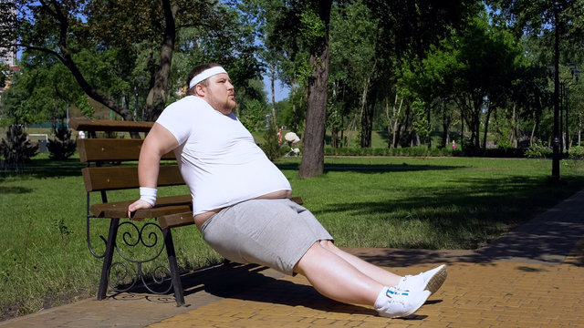 Obese young man exercising on bench, outdoor workouts, struggle to slim down - Powered by Adobe