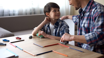 Father playing toy cars with his smiling son, parental care, togetherness