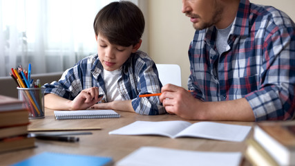 Father and son doing homework together, dad explaining task, school education