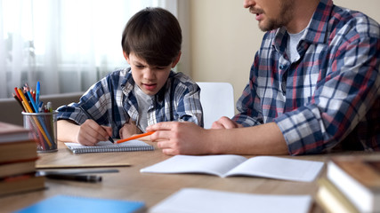 Dad sitting at the table and making his capricious son to do homework, education