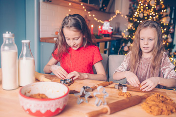 Little girls making Christmas gingerbread house at fireplace in decorated living room.