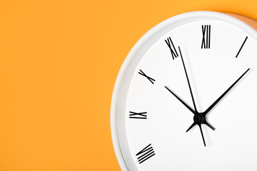 White round clock with black numbers isolated on yellow orange wall. Time background.
