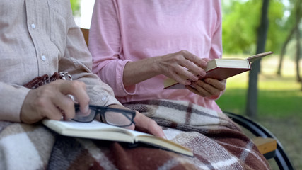 Mature husband and wife resting on garden bench covered blanket, reading books