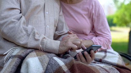 Obraz na płótnie Canvas Retired couple browsing smartphone program, sitting in park, online application