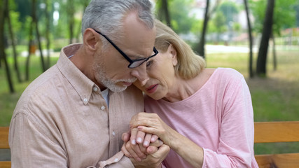 Fototapeta premium Male pensioner comforting sick elderly wife, sitting in hospital garden together