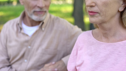 Handsome pensioner looking at pretty mature woman with interest sitting in park