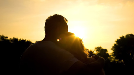 Silhouette of old hugging couple, watching sunset together, secure old age