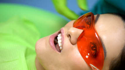 Woman patient in protective glasses, curing light for modern teeth treatment
