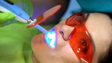 Patient in protective red glasses during treatment with blue curing light