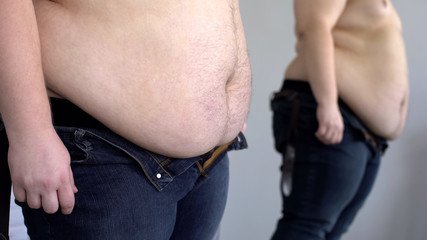 Overweight male looking at fat belly mirror reflection, obesity health problem