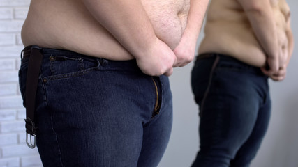 Obese man trying to button up jeans, overweight problem, unhealthy lifestyle