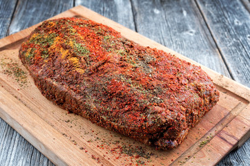 Traditional raw pulled pork piece of Bosten butt with spicy rub as closeup on a wooden cutting board