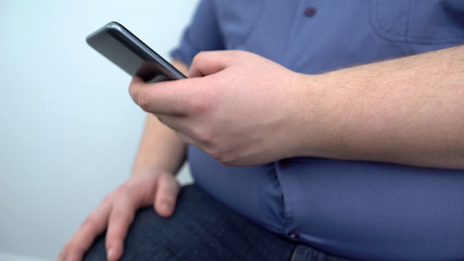Overweight man typing smartphone message, fitness training program online, diet