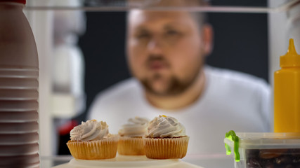 Hungry fat man looking at cream cakes in fridge at night, diabetes risk, sugar