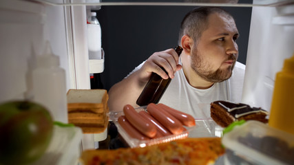 Fat male secretly taking beer bottle from fridge at night, unhealthy lifestyle