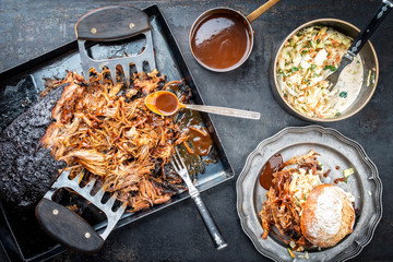 Traditional barbecue pulled pork piece of Bosten butt torn to bits with coleslaw and burger as top view on a board