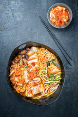 Traditional Korean kimchi jjigae with grilled pork belly and ramen as closeup in a modern design Japanese cast-iron roasting dish